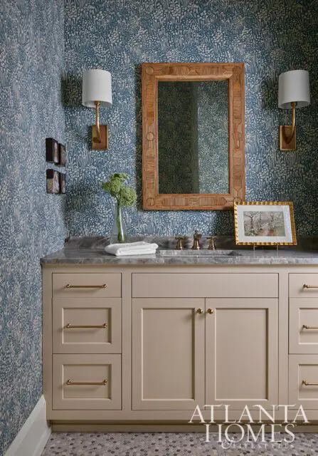 Blue floral wallpaper, wood mirror, and beige vanity with brass hardware.