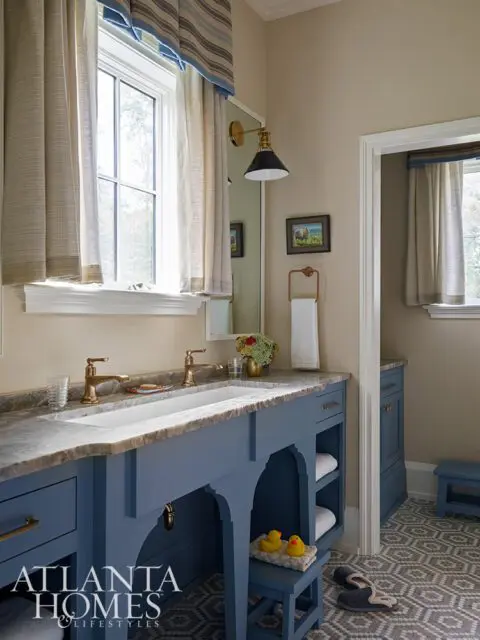Blue vanity with marble countertop, brass faucets, and arched open shelving.