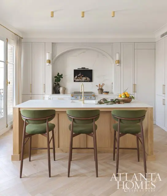 Kitchen island with green bar stools, white marble countertop, and wood cabinetry.