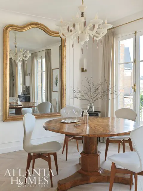 Dining room with round wood table, upholstered chairs, and large gold mirror
