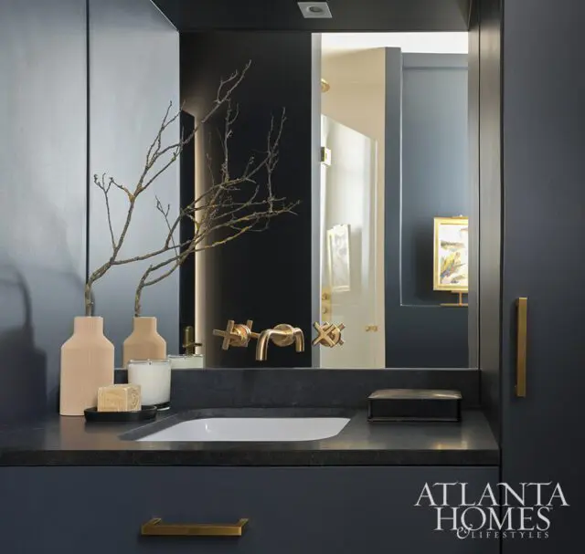 Dark blue vanity with stone countertop, brass faucet, and decorative branches.