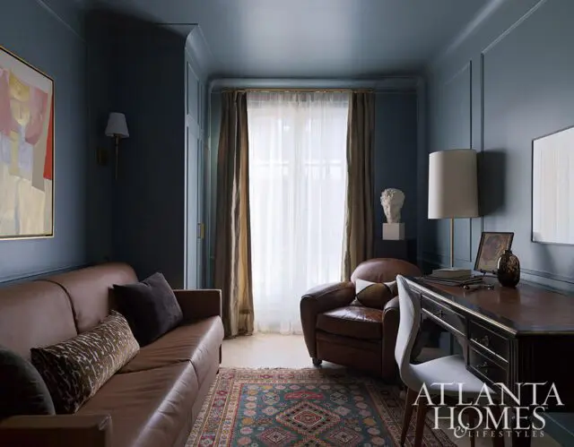Dark blue room with brown leather sofa, armchair, and desk. Oriental rug on floor.