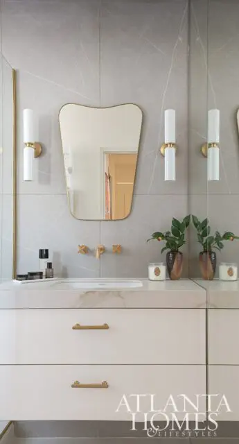 Modern bathroom vanity with white drawers, gold hardware, marble countertop, and gray tile walls.