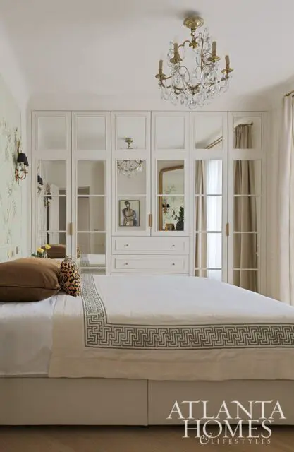 Bedroom with mirrored closet doors, crystal chandelier, and Greek key trim on bedding.