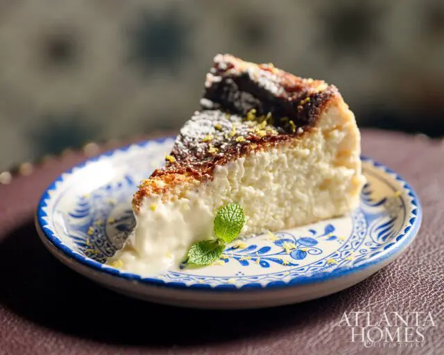 Slice of cheesecake with burnt top, dusted with powdered sugar and lemon zest, on a blue and white