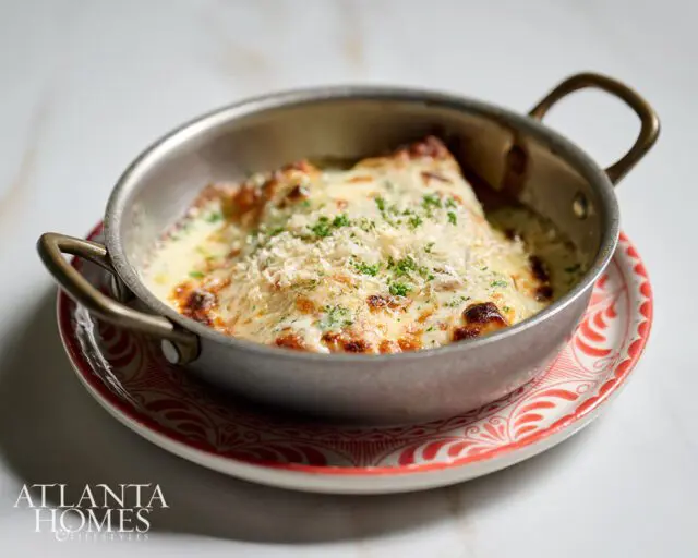 Baked pasta dish with melted cheese and parsley in a metal pan on a decorative plate.