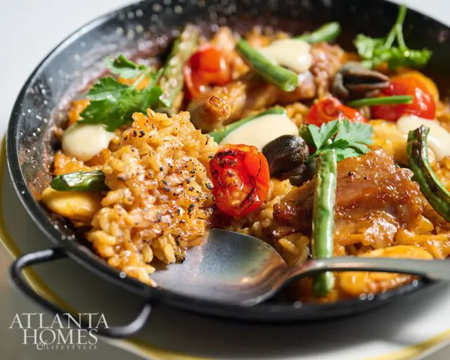 Paella with rice, chicken, tomatoes, green beans, and mushrooms in a black pan.