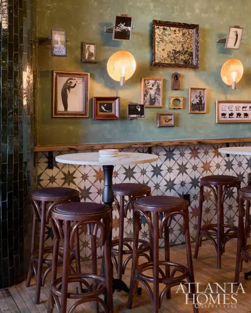 Green wall with framed art, round lights, and bar stools in front of a patterned tile backsplash.