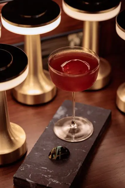 Red cocktail with ice sphere and decorative chocolate on dark slate
