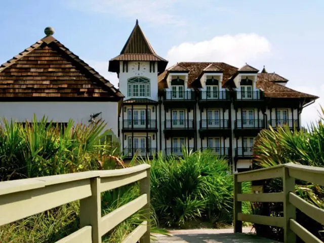 White building with dark balconies and dormer windows, topped with a clock tower and shingled roof.