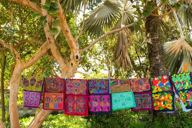 Colorful textile art with geometric and animal designs hanging on a clothesline between trees.