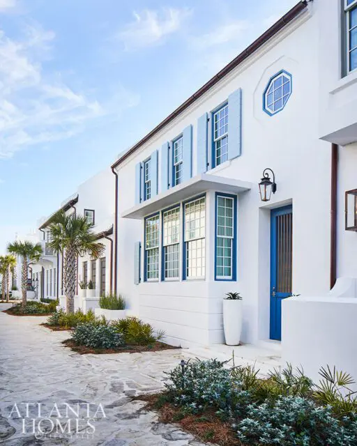 White building with blue shutters and door, palm trees, and stone walkway