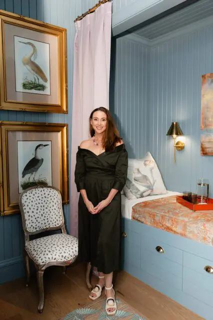Woman in dark green dress standing by a blue built-in bed with orange patterned bedding.