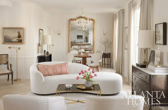 Living room with a curved white sofa, pink accent pillow, and a gold-framed mirror reflecting a
