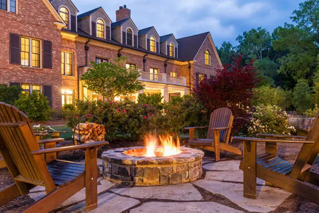 Stone firepit with Adirondack chairs and a brick building at dusk
