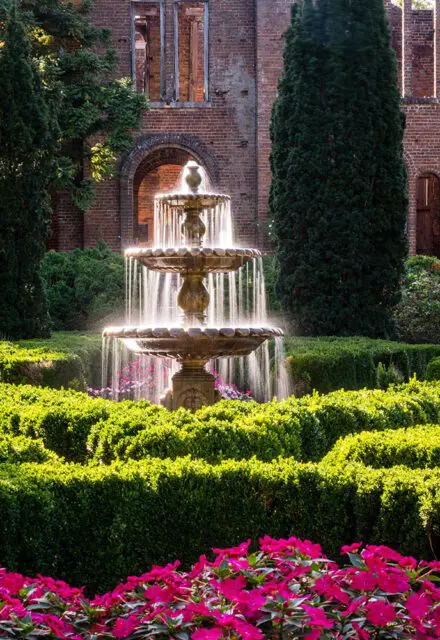 Tiered fountain in a formal garden with manicured hedges and pink flowers