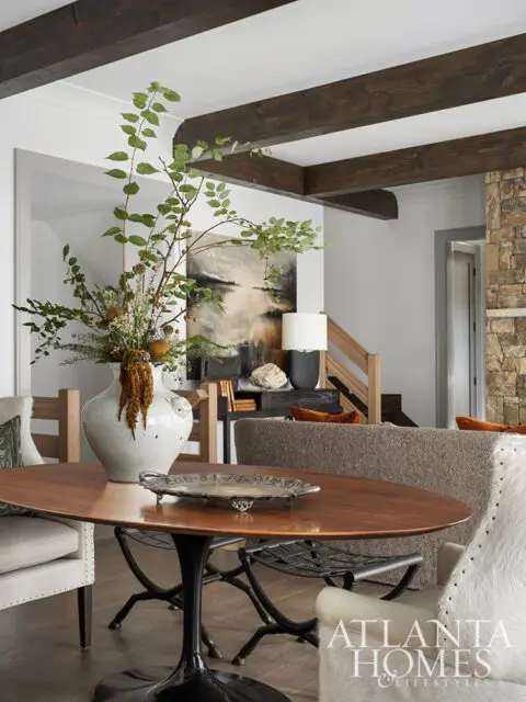 Oval wood dining table with large vase of greenery, silver tray, and chairs.