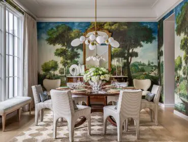 Dining room with scenic mural wallpaper, striped chairs, and a round wooden table.