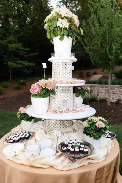 Dessert table with cupcakes and flowers, set outdoors.