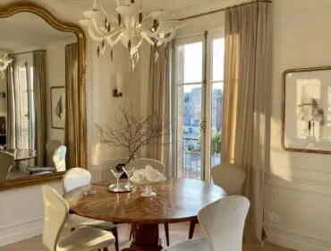 Dining room with round wood table, cream upholstered chairs, and large gold mirror.