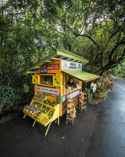 Yellow fruit stand with pineapples, avocados, and bananas. Signage for shave ice and smoothies.