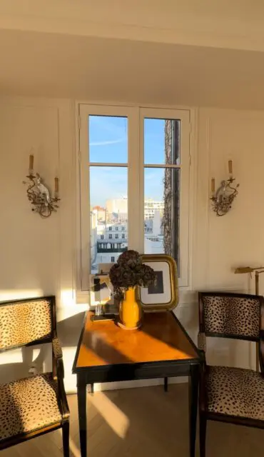 Two chairs with leopard print upholstery flank a table with a yellow vase and framed art.