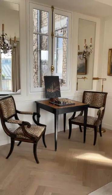 Room with two chairs upholstered in leopard print fabric, a table with a chessboard, and a painting.