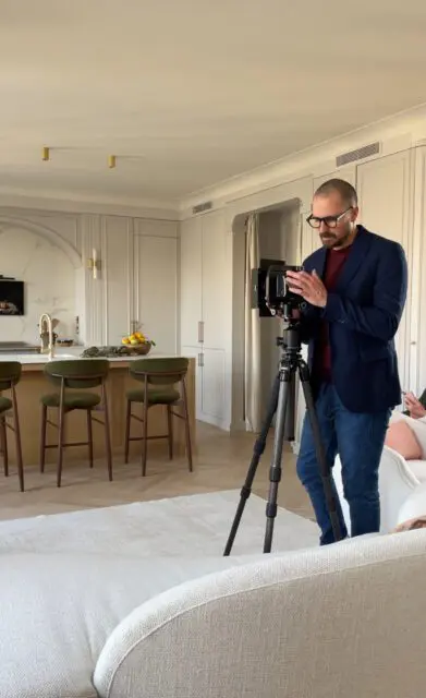 Man with camera on tripod in modern kitchen with island and green stools