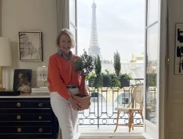 Woman holding potted olive tree in apartment with Eiffel Tower view