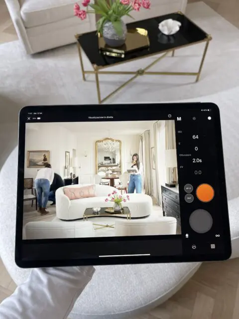 Tablet displaying a living room with two people, a white sofa, and a black coffee table. Camera