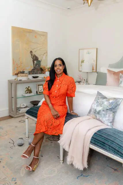 Woman in orange dress sitting on bench in bedroom with large artwork and bed