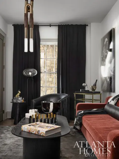 Living room with a rust-colored sofa, black armchair, black curtains, and a coffee table with a