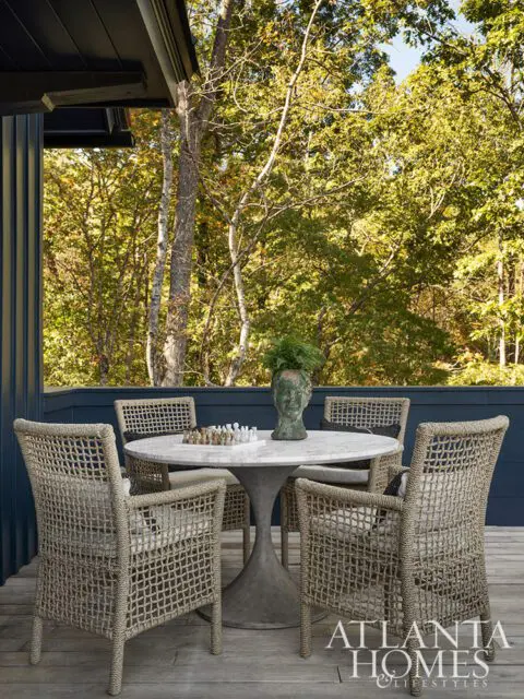 Woven chairs around a marble table on a wooden deck with trees in the background.