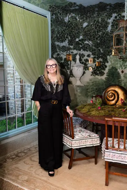 Woman in black standing in dining room with tree mural wallpaper and moss-covered table