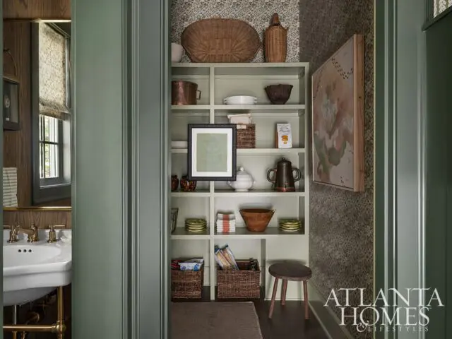 Pantry with sage green shelves, woven baskets, copper pots, and framed art.