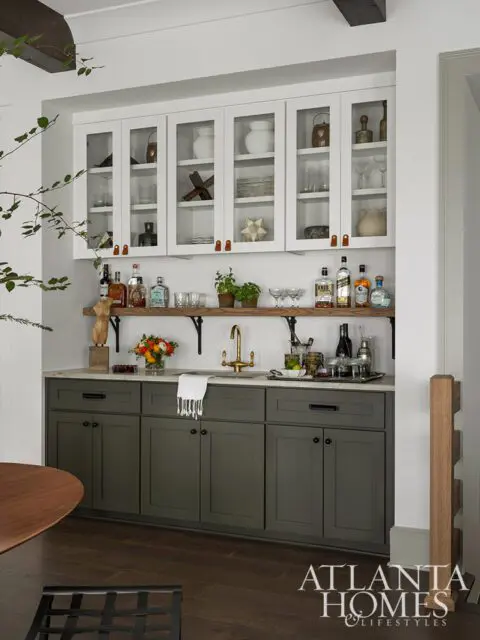 Bar area with white glass-front cabinets, dark green base cabinets, marble countertop, and brass