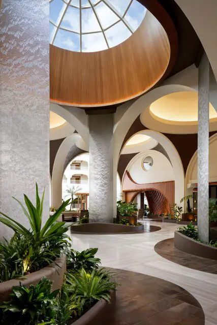 Lobby with curved arches, wood accents, and lush plants under a domed skylight.