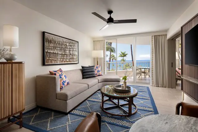 Living room with sectional sofa, blue geometric rug, rattan coffee table, and ocean view balcony.