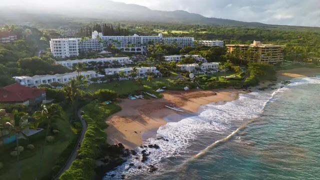 Resort buildings on a tropical coastline with a sandy beach and ocean waves.