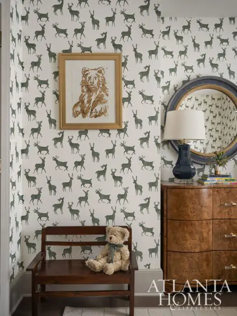 Room with deer print wallpaper, wooden bench with teddy bear, framed bear art, and burl wood