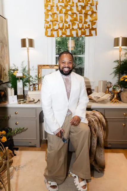 Man in white blazer and tan pants sitting in a room with decorative items.