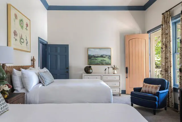 Bedroom with two queen beds, blue door, peach door, and blue armchair.