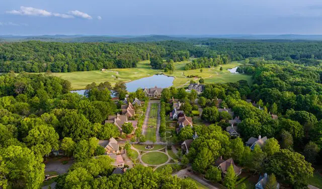 Aerial view of a village with houses, a lake, and a golf course surrounded by trees.