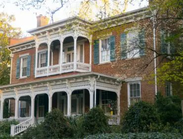 Brick house with white ornate porches and green shutters.