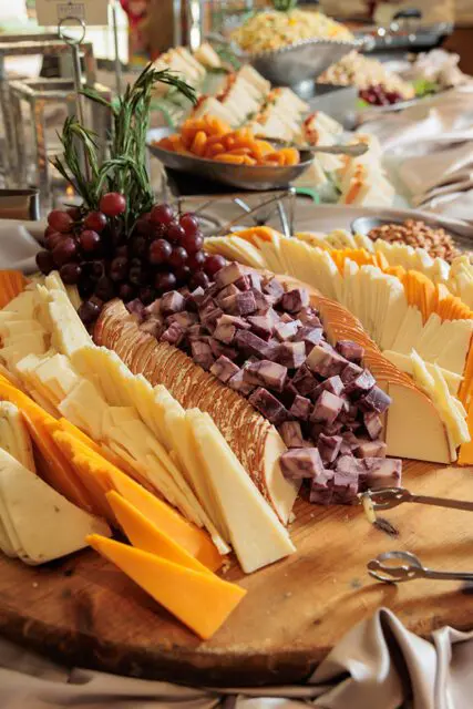 Wooden board with sliced cheeses, grapes, rosemary, and crackers
