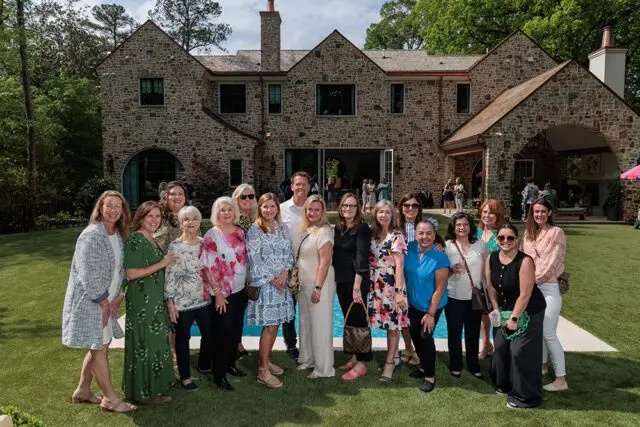 Stone mansion with group of people posing on lawn in front of pool