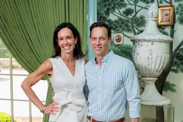 Woman in white dress and man in blue gingham shirt smile in front of green curtains and chinoiserie