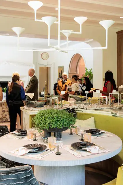 Round dining table set with black plates and glassware, green banquette seating in background.