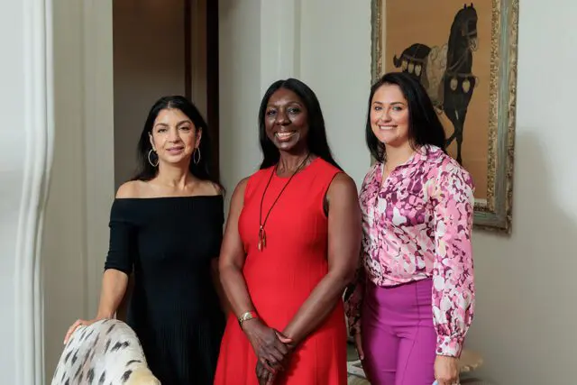 Three women smiling, one in black off-the-shoulder dress, one in red dress, one in pink floral