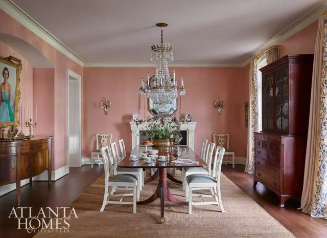 Dining room with pink walls, crystal chandelier, fireplace, and dark wood furniture.